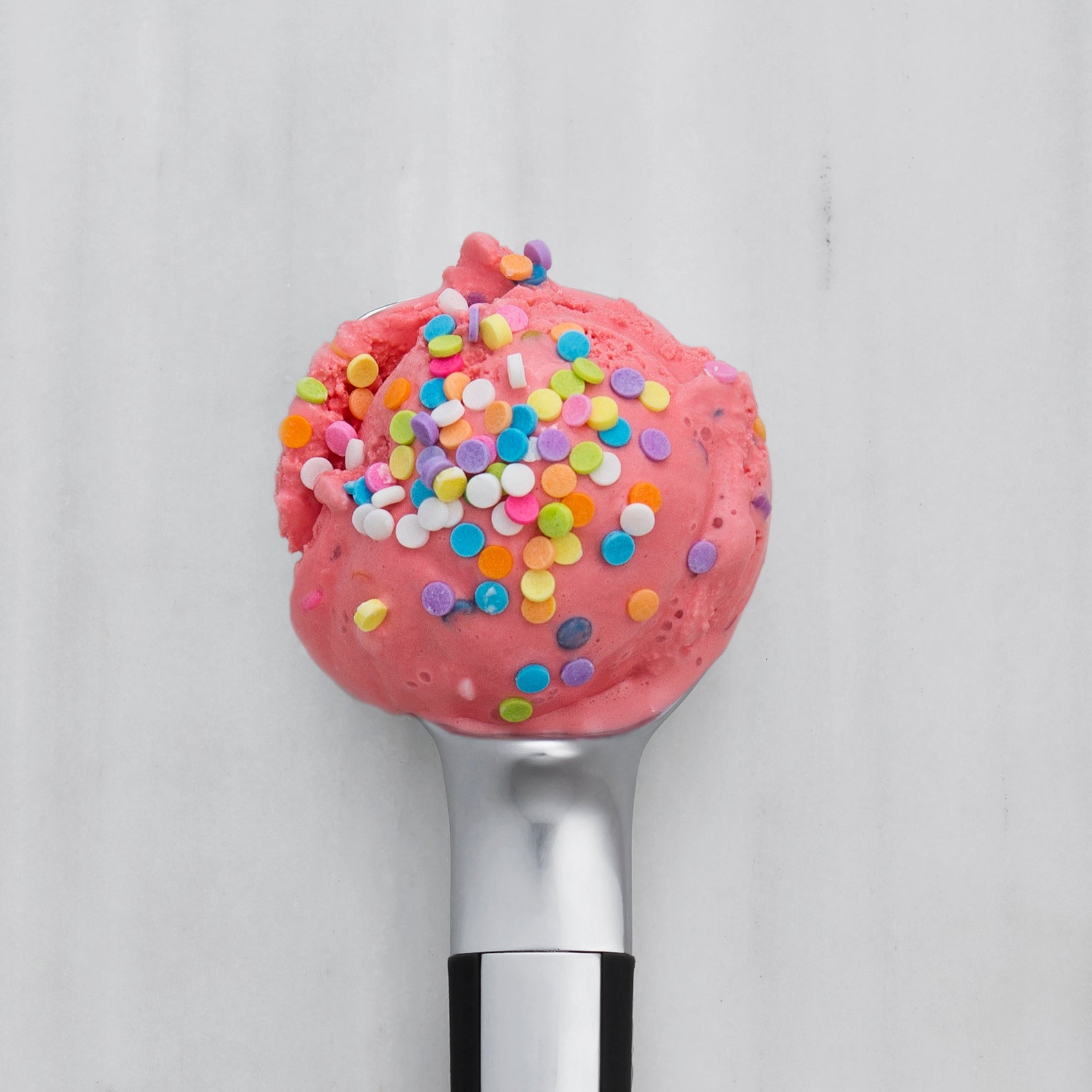 Pink ice cream with colorful sprinkles on a silver spoon 