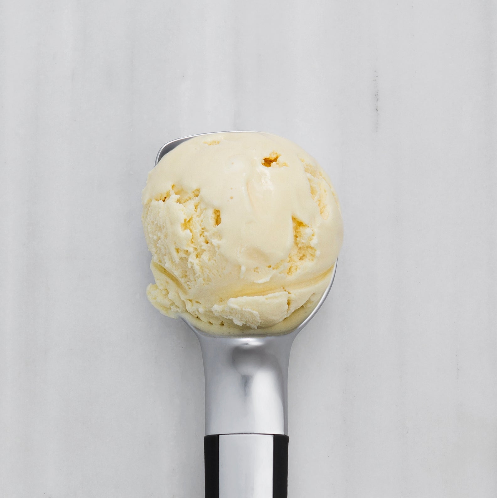 Ice cream scoop with a scoop of vanilla ice cream on a light gray background