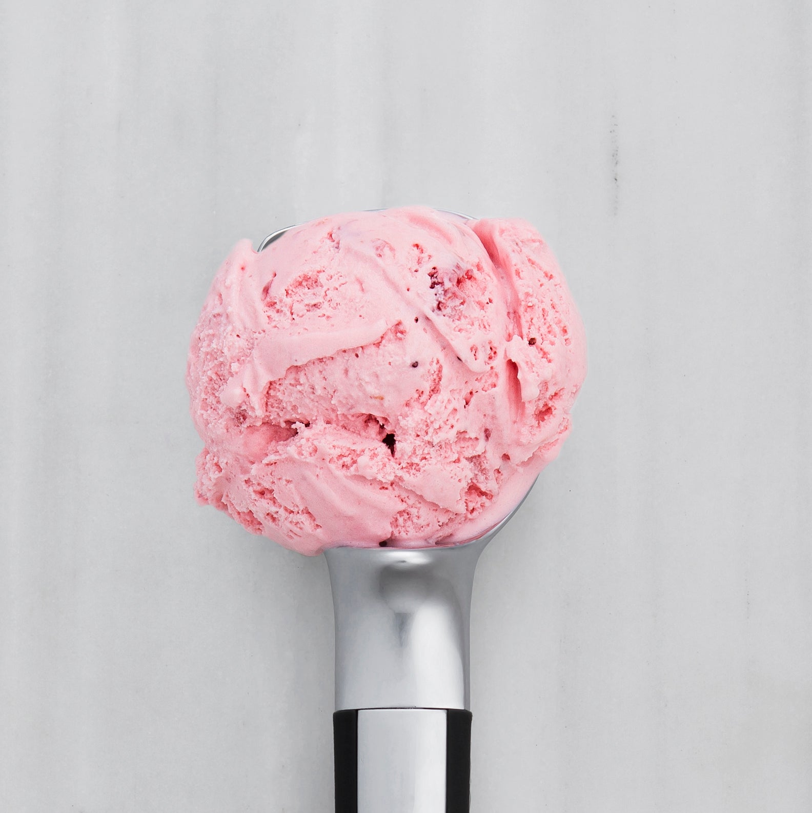 Strawberry ice cream  in a metal scoop on a light gray background